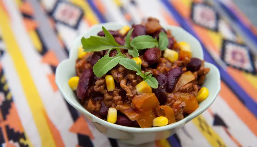 Miseczka pełna aromatycznego chili con carne przepis oryginalny, z fasolą, kukurydzą i mięsem mielonym, ozdobiona świeżymi ziołami.