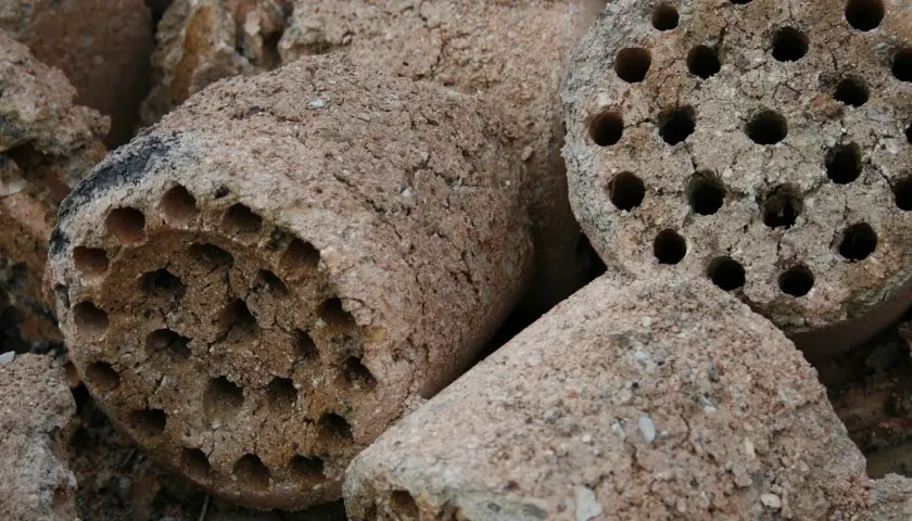 Brykiety z węgla brunatnego, gotowe do użycia. Pokazują, jak działa brykieciarka, sprasowując materiał w cylindryczne kształty z otworami.