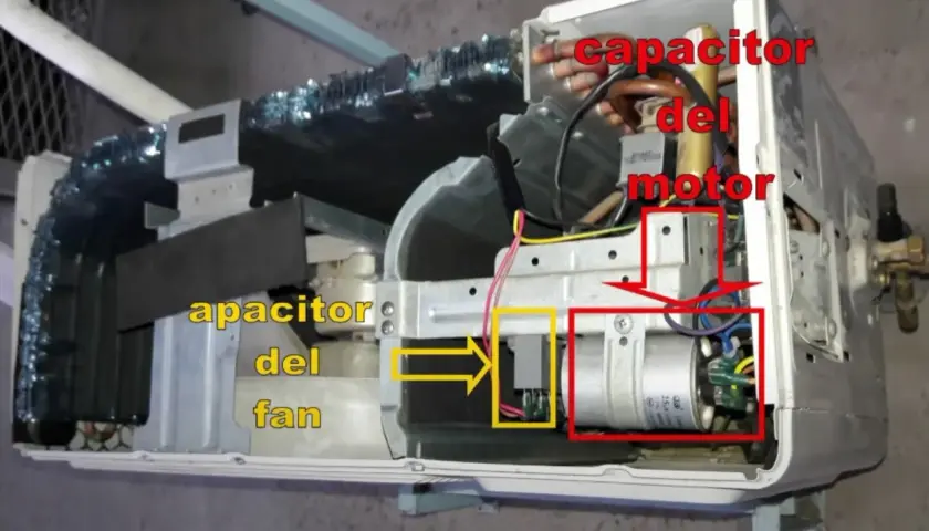 Componentes internos de un aire acondicionado, mostrando el capacitor del motor y el capacitor del fan.