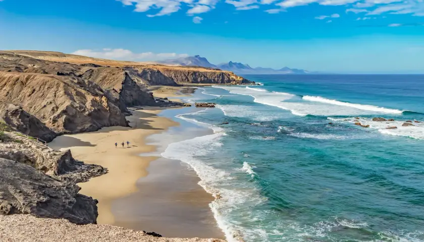Fuerteventura lipiec: słoneczna pogoda, turkusowe morze i piaszczysta plaża z klifami. Idealne warunki dla surferów.
