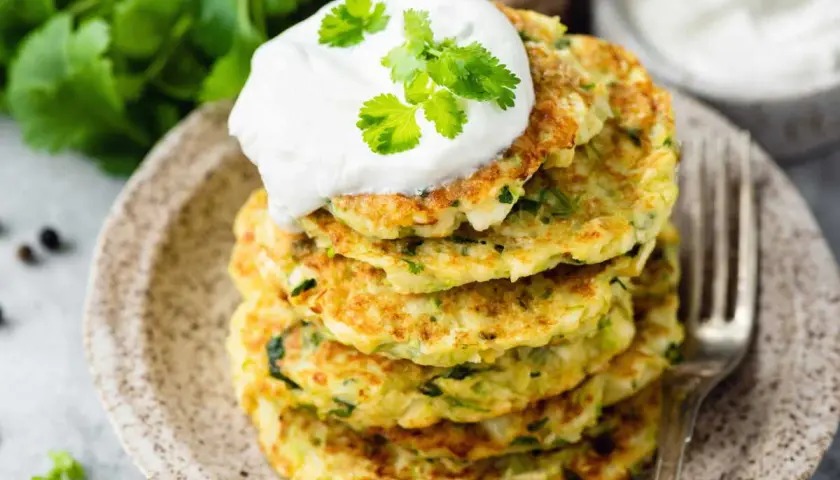 Pile de beignets de courgettes à l'italienne, garnis d'une cuillère de crème et de coriandre fraîche. Un délice croustillant et savoureux.