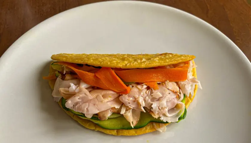 Piadina di ceci ripiena di tacchino sfilacciato, zucchine e carote a julienne. Un pasto leggero e gustoso.