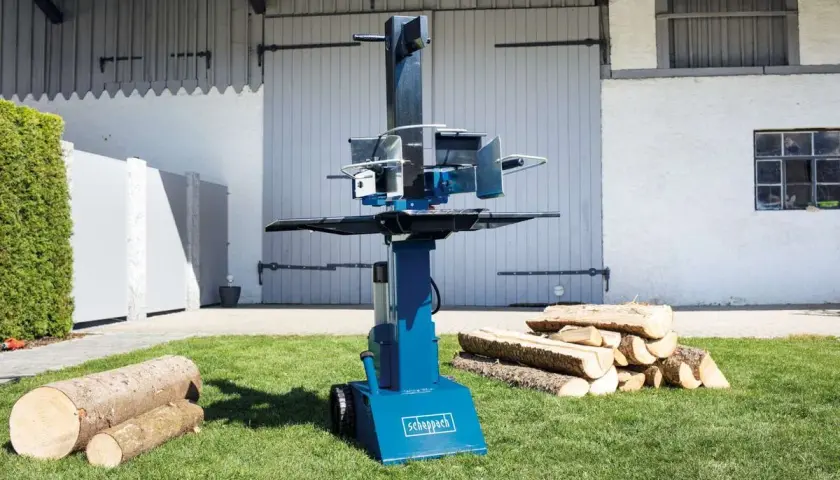 Scheppach Holzspalter Öl nachfüllen: Ein blauer Holzspalter steht auf einem Rasen, daneben liegen Holzscheite.