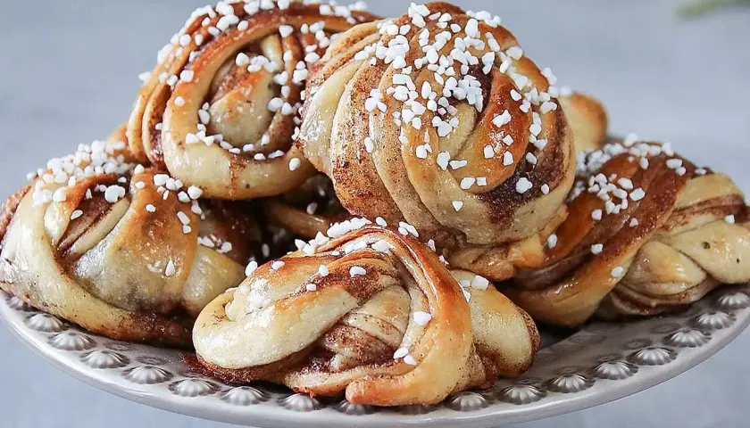 En hög med laktosfria kanelbullar, toppade med pärlsocker, ligger på ett fat.