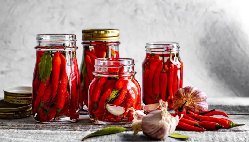 Słoiki z papryczkami chili w zalewie, obok czosnek i świeże papryczki. Idealne do pikantnych potraw.