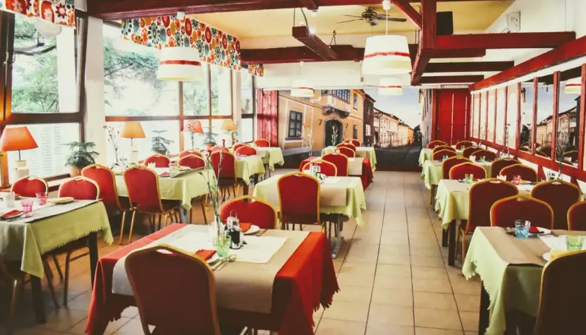 Wnętrze restauracji z czerwonymi krzesłami i stolikami nakrytymi na przyjęcie. Mural z ulicą przypomina czardasz Gdańsk.
