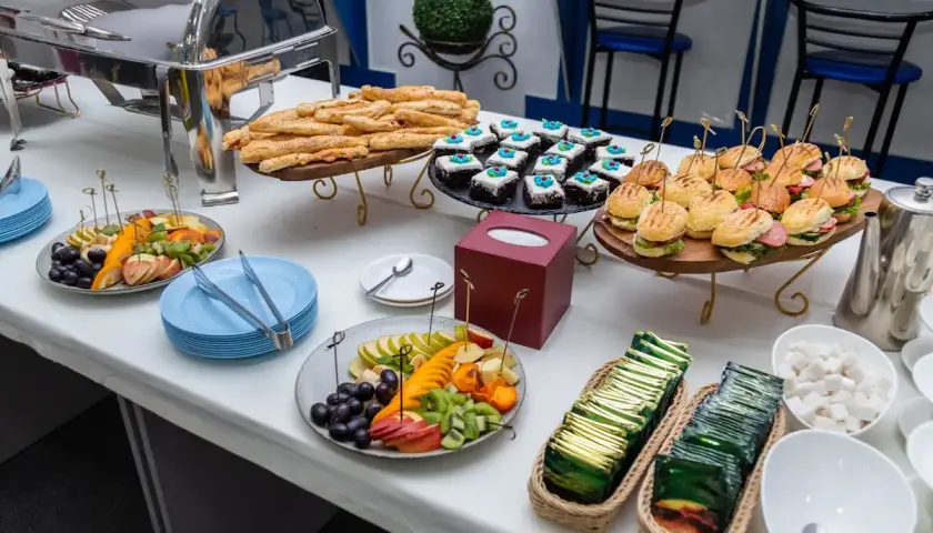 Un buffet de hors d'œuvre varié avec mini-burgers, pâtisseries, bâtonnets feuilletés et salade de fruits.