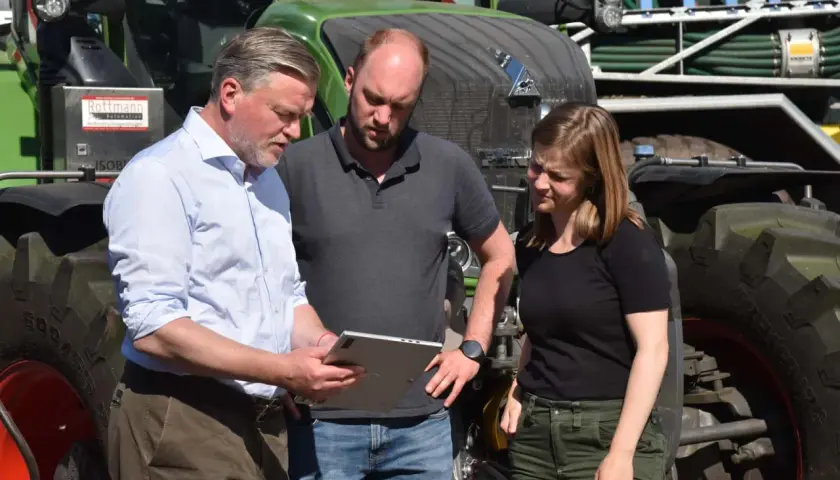 Drei Personen besprechen auf einem Tablet die **Pauschalierung in der Landwirtschaft** vor einem grünen Traktor.