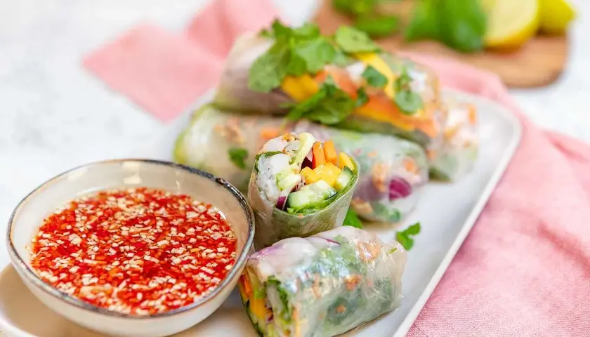 Färska vietnamesiska vårrullar fyllda med grönsaker och räkor, serverade med en röd dippsås.