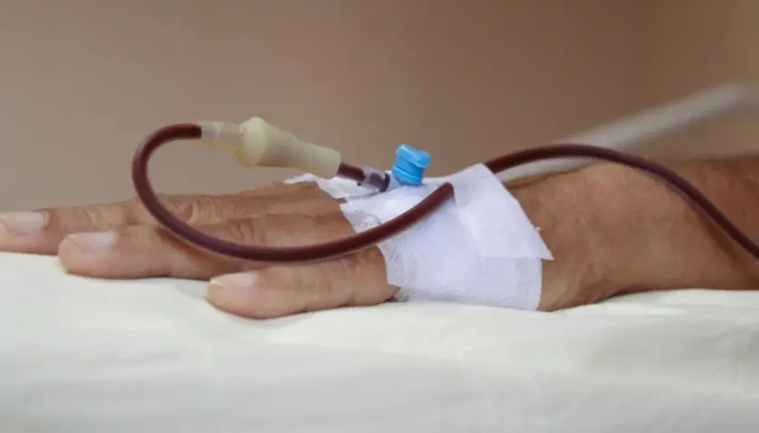 Dłoń pacjenta z założonym wenflonem i podłączoną czerwoną rurką do transfuzji.