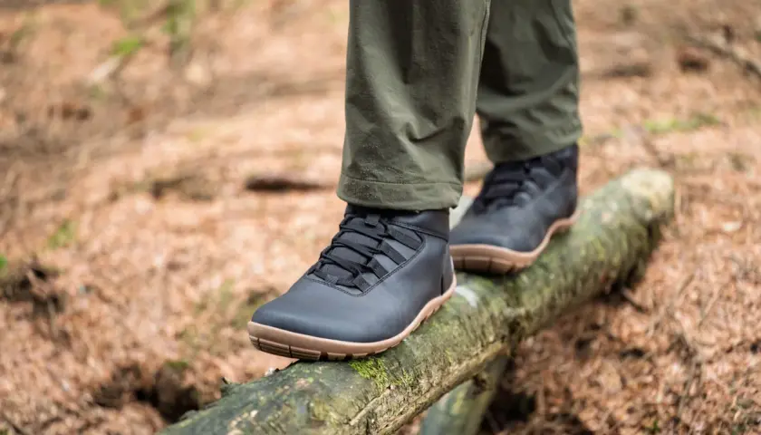 Black, low-profile shoes with tan soles, perfect as shoes to wear in winter besides boots, balance on a mossy log in a forest.