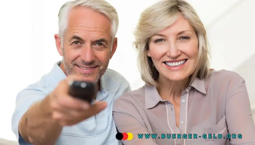 Glückliches Rentnerpaar mit Fernbedienung. Informieren Sie sich über die GEZ-Befreiung für Rentner und die Einkommensgrenze auf www.buerger-geld.org.