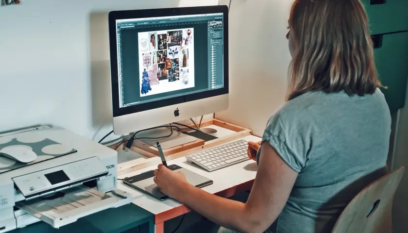 Une graphiste textile travaille sur son ordinateur, créant des moodboards et des designs. Une imprimante est visible à côté.