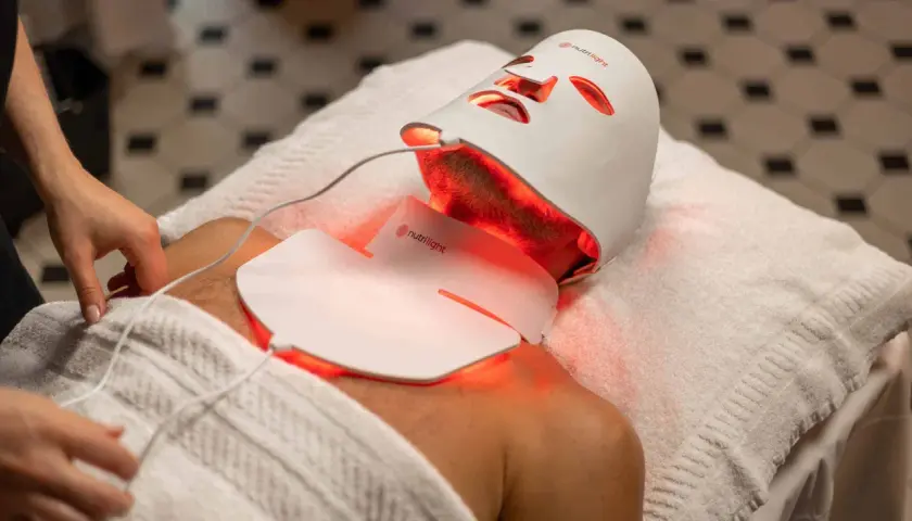 En person får behandling med en vit led mask ansikte som lyser rött.