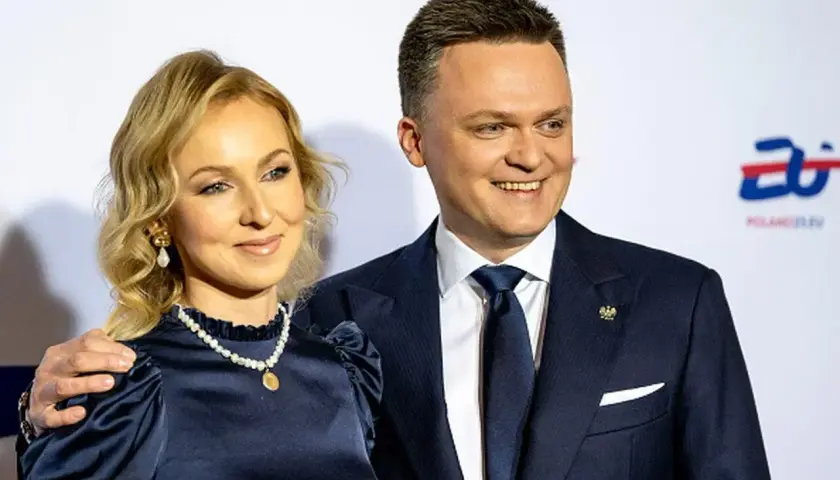 Szymon Hołownia z żoną, uśmiechnięci, pozują do zdjęcia. Ona w granatowej sukience i perłach, on w garniturze.