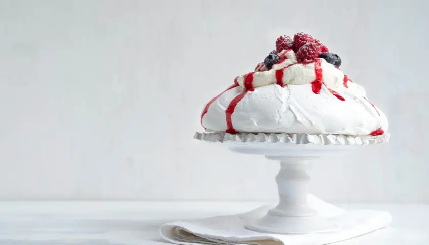 En vacker pavlova i långpanna, toppad med grädde, bär och röd sås.