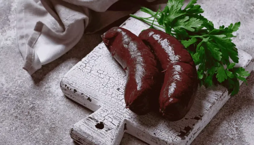 Deux boudins noirs sur une planche en bois, prêts à être cuits. Apprenez comment cuire le boudin noir sans qu'il éclate pour un plat parfait.