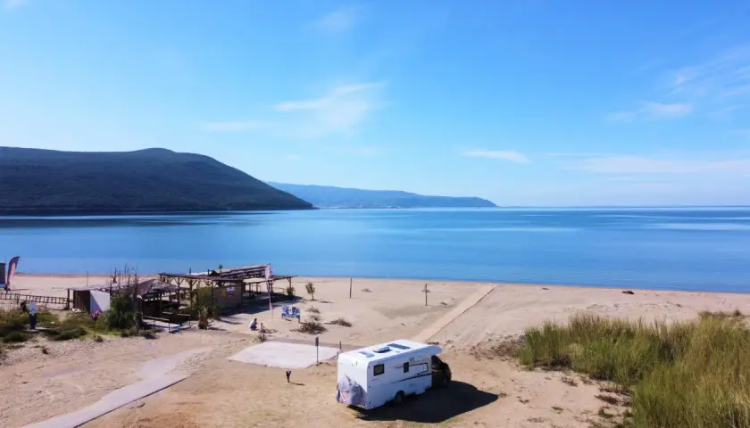 Kamper na piaszczystej plaży w Grecji kontynentalnej, z widokiem na spokojne morze i zalesione wzgórza. Idealne miejsce na wakacje.
