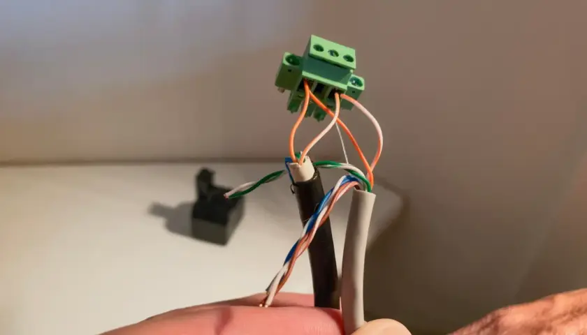 Connexion de fils électriques à un domino vert. Un câble noir et un câble gris sont dénudés, leurs fils colorés prêts pour le domino.