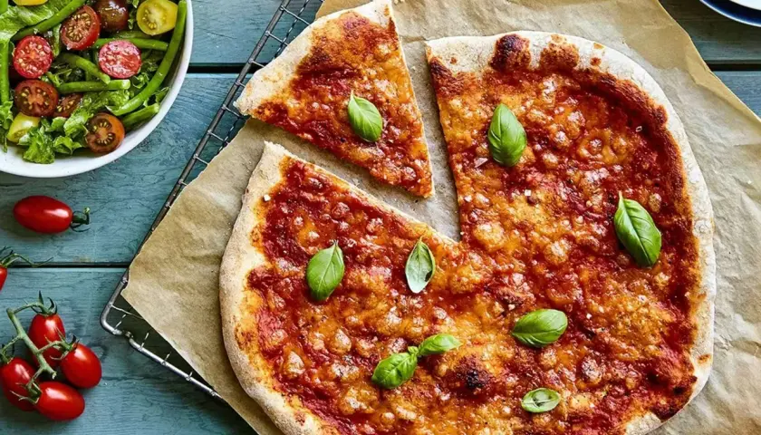 En nybakad liba pizza med tomatsås och basilika, serverad med en fräsch sallad.