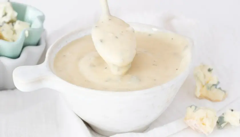 Cremosa salsa gorgonzola servida en un cuenco blanco, con trozos de queso gorgonzola esparcidos alrededor.