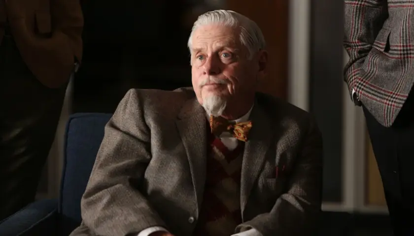 Äldre man med grått hår och bockskägg, klädd i kavaj och fluga. Robert Morse ser fundersam ut.