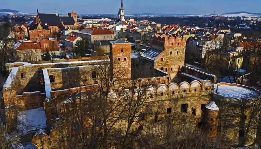 Ruiny zamku w Ząbkowicach Śląskich, z charakterystycznymi ceglanymi murami i wieżami, na tle zimowego krajobrazu miasta.