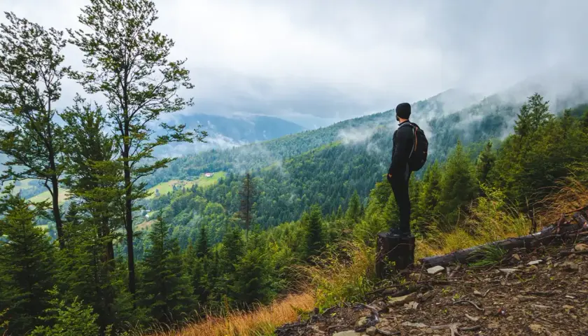 Mężczyzna z plecakiem podziwia widok na górzyste tereny podczas **hiking po polsku**. Mgła spowija szczyty, tworząc malowniczy krajobraz.