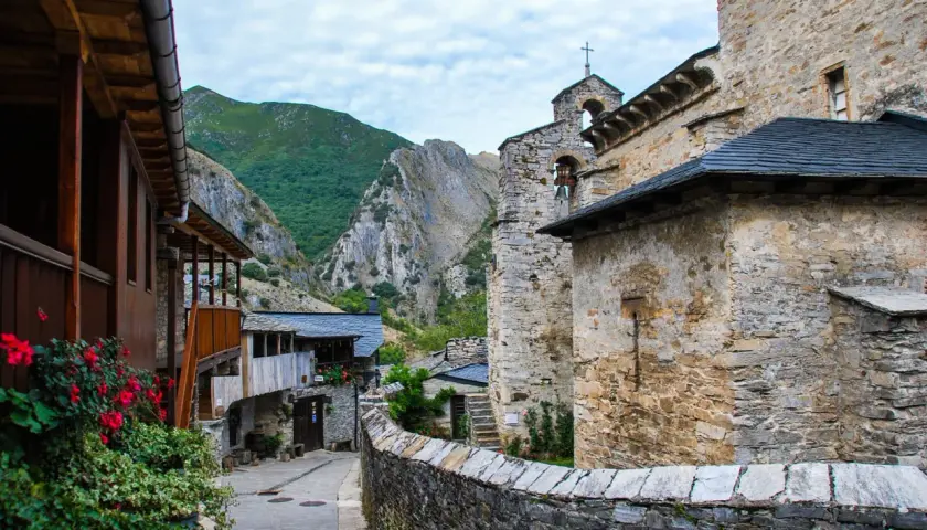 Un pueblo de piedra y madera se alza en el valle del silencio, rodeado de montañas verdes y un cielo nublado.