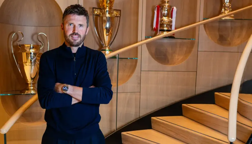 Erik ten Hag, trener Manchester United, stoi na tle pucharów, symbolizujących sukcesy klubu.