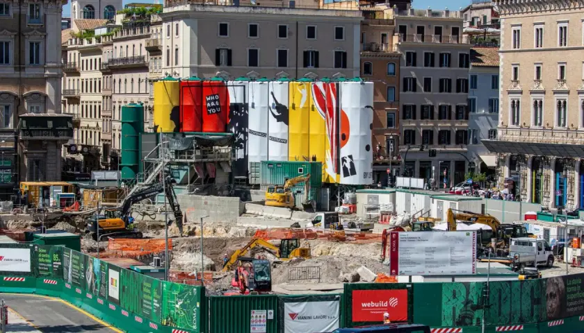Cantiere per i lavori metro Roma con grandi teli colorati e macchinari edili.