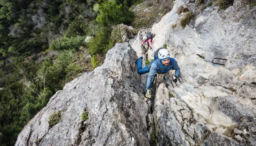 Mann klettert gesichert im Klettersteig, die Rastschlinge ist am Gurt befestigt.
