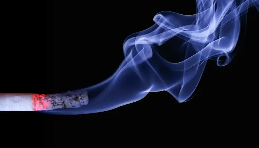 Fumo bluastro si alza da una sigaretta accesa, un'immagine che evoca il pericolo del fumare in allattamento.