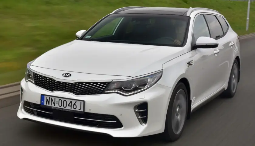 Biała Kia Optima w wersji kombi na drodze. Wiele osób szuka kia optima opinie przed zakupem.