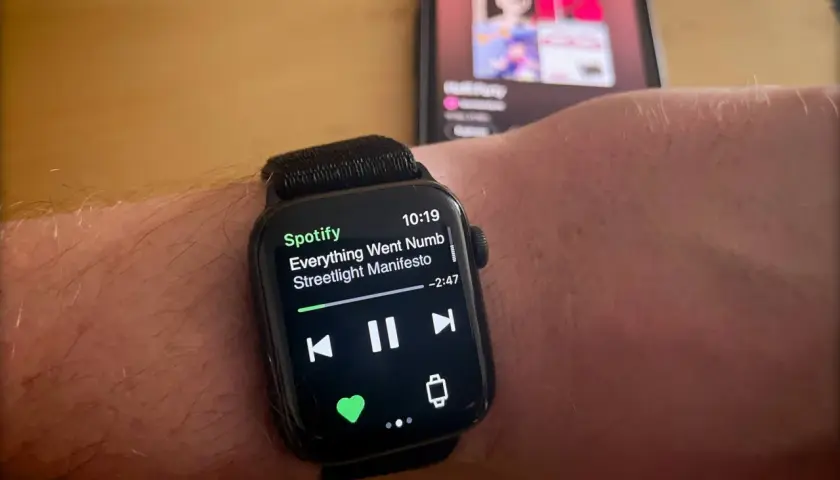 Apple Watch zeigt Spotify-Song "Everything Went Numb" von Streetlight Manifesto. Ein iPhone im Hintergrund spielt ebenfalls Musik.