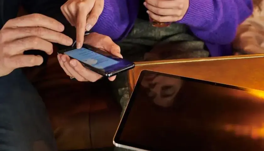 Dłonie pokazują, jak zwiększyć litery w telefonie. Obok leży tablet.