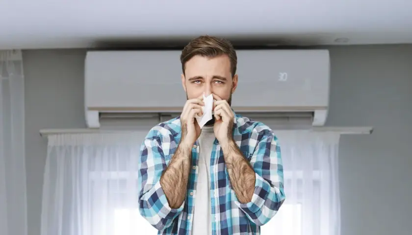 Hombre con pañuelo en la nariz, con aire acondicionado de fondo. Podría ser que se puede tener alergia al aire acondicionado.
