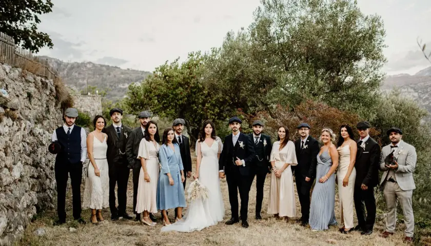 Mariage Peaky Blinders : le couple et leurs témoins, tous habillés de costumes d'époque, posent devant un paysage rocheux et verdoyant.