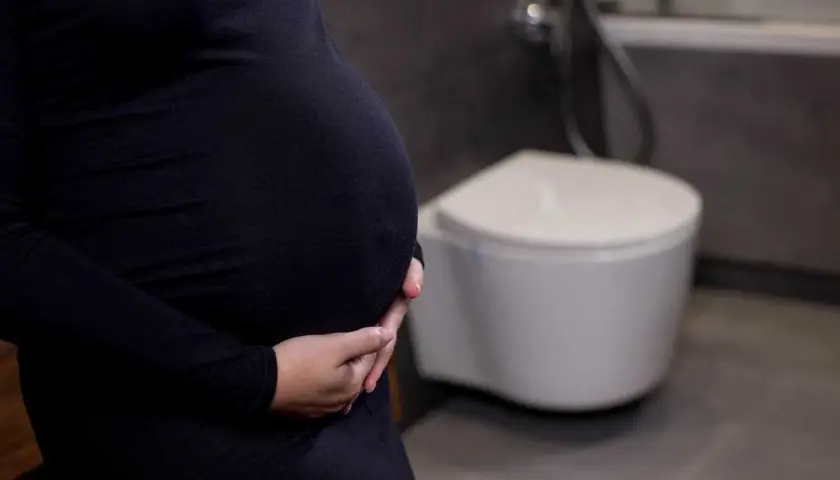 Gravid kvinna med händer på magen, toalett i bakgrunden. Vanliga besvär som uvi kan drabba gravida.