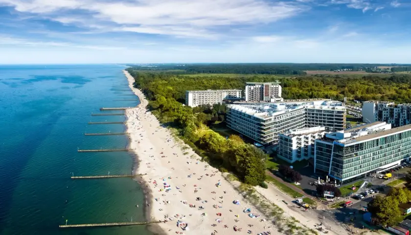 Fajny hotel nad morzem z widokiem na piaszczystą plażę pełną wypoczywających ludzi i turkusową wodę.