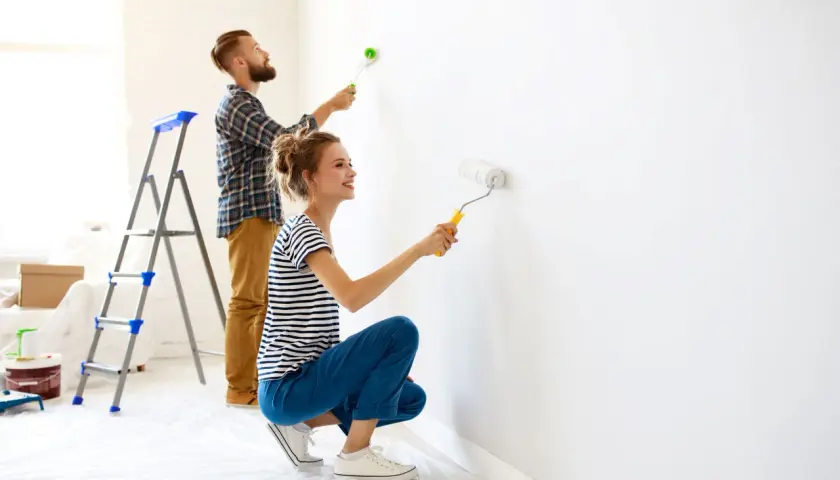 Coppia felice imbianca casa con rullo, trasformando le pareti bianche in un nuovo inizio.