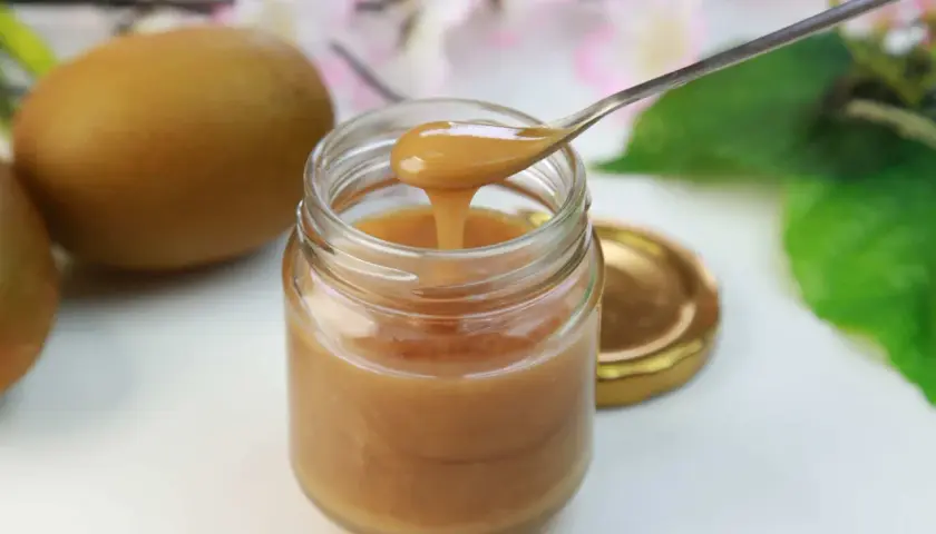 Gęsty, złocisty miód manuka na łyżeczce, obok owoców kiwi. Odkryj niezwykłe miód manuka właściwości.