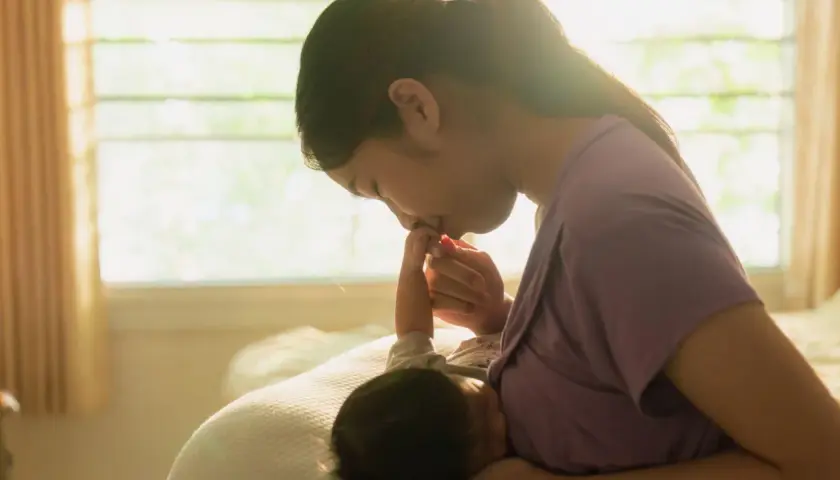 Dolce momento tra madre e neonato. La mamma bacia la manina del suo piccolo, che sembra aver mangiato troppo, sazio e felice.