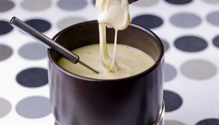 Un morceau de pain trempé dans une fondue au comté crémeuse, filant sur une fourchette.