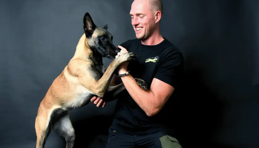 Ein Mann lacht und hält die Pfoten seines Malinois. Erfolgreiches Hunde Training zeigt die enge Bindung.