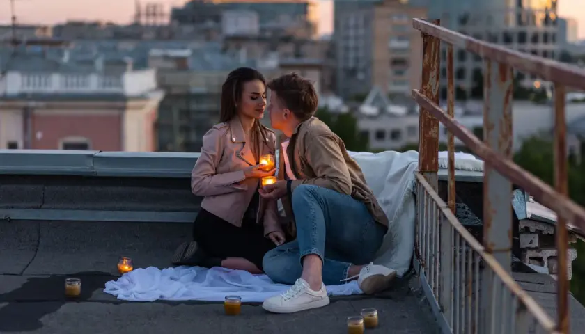 Romantyczny wieczór na dachu. Para trzyma świece, patrząc sobie w oczy. Czy napisać pierwsza do faceta?