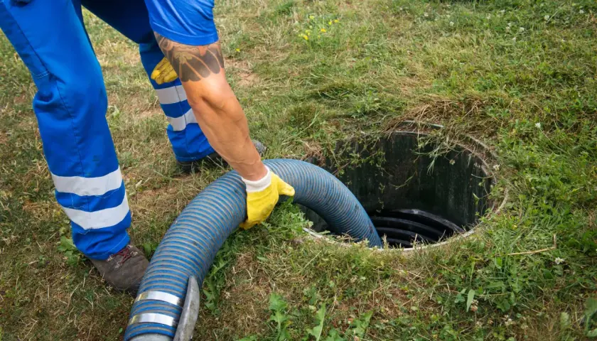 Pracownik w żółtych rękawiczkach wkłada gruby wąż do szamba, pokazując, jak zrobić odpływ.