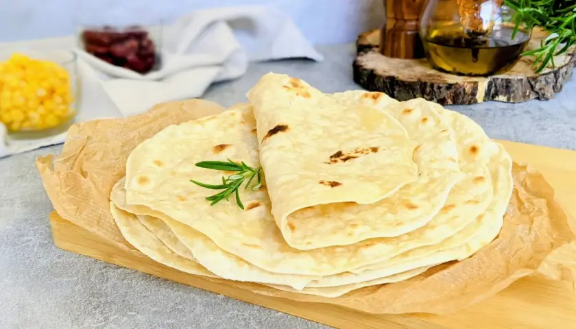 Stos świeżo upieczonych tortilli, idealnych do przygotowania najlepszej tortilli z ulubionymi dodatkami. Gałązka rozmarynu dodaje aromatu.
