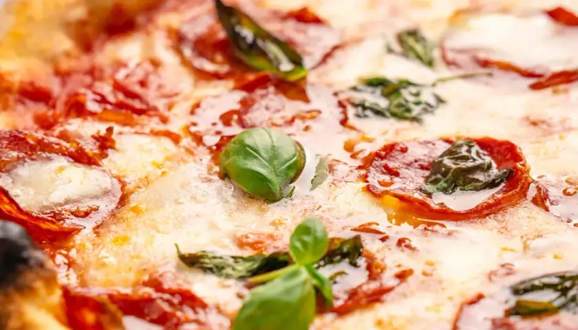 Nahaufnahme einer Pizza mit geschmolzenem Käse, roten Salami-Scheiben und frischem Basilikum. Verschiedene Salami-Sorten machen diese Pizza unwiderstehlich.
