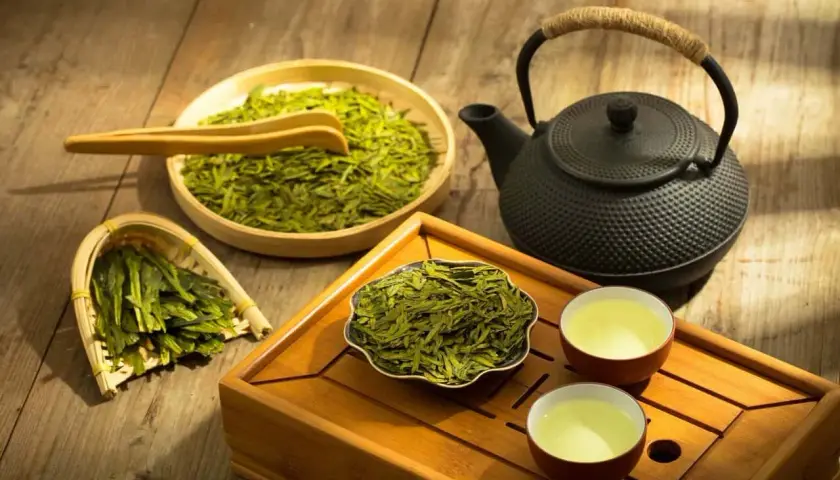 Zaparzanie sencha green tea. Suszone liście, czajniczek i dwie filiżanki z naparem na drewnianej tacce.